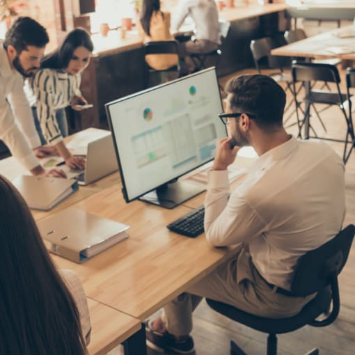 Group of young professionals work and collaborate on desktop computers in an open office.