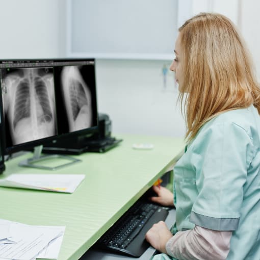 Medical professional in blue scrubs uses Acuo VNA to view medical images on a desktop computer.