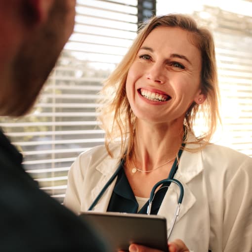 Medical professional wearing a white coat and stethoscope holds a tablet computer and smiles.
