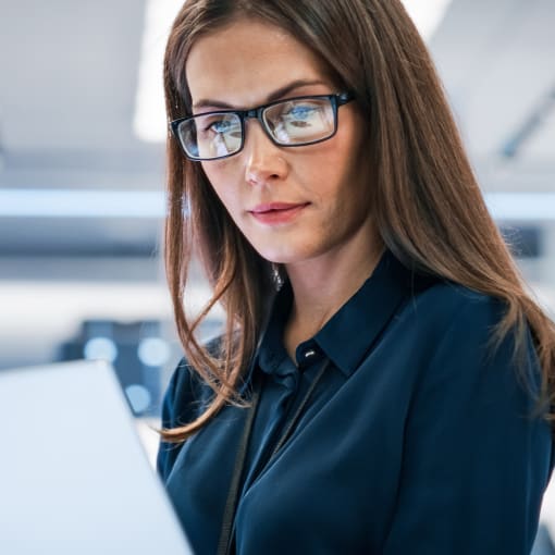 Person in glasses works on a laptop in a modern office.