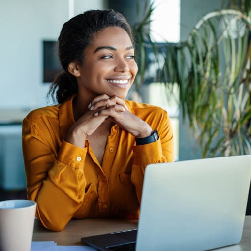 Person smiles and sits in front of a laptop computer and coffee mug.