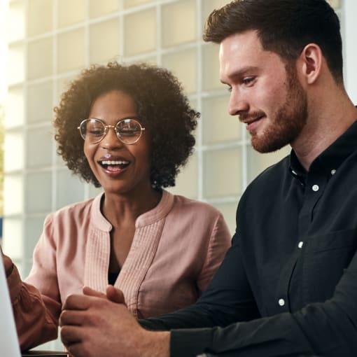 Two people smile while collaborating on a laptop computer.