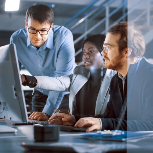 Three young professionals collaborate at a desktop computer.