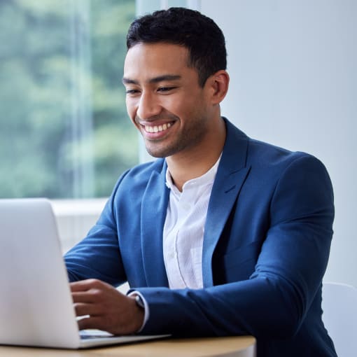 Person in blue suit sits at a small desk, working on a laptop.