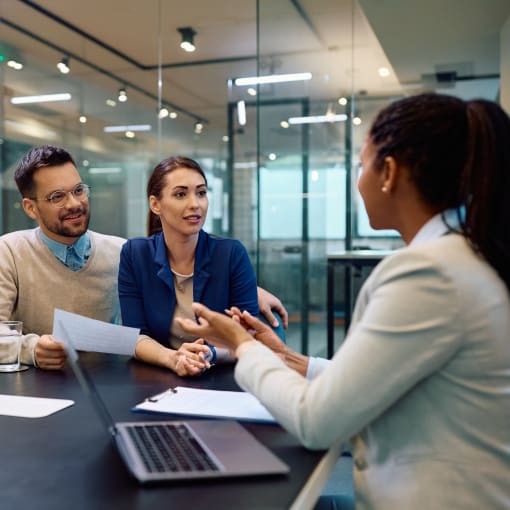 A couple discussing with a young professional in a corporate setting.