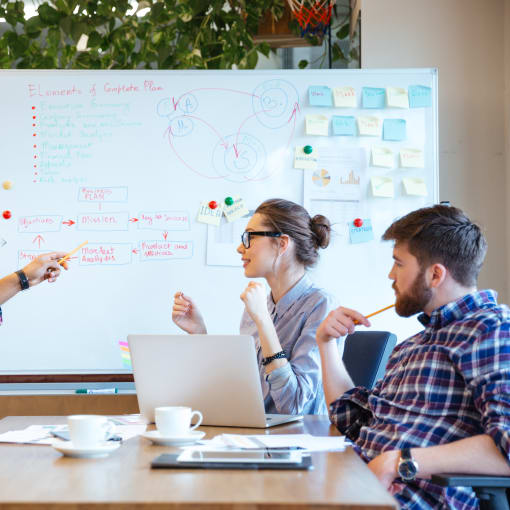 A group of young professionals having an active discussion using a whiteboard.