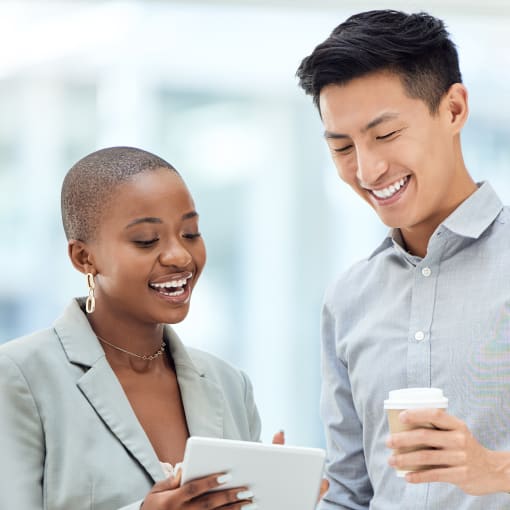 Two people smile and look over information on a notebook. One is holding a cup of coffee. 