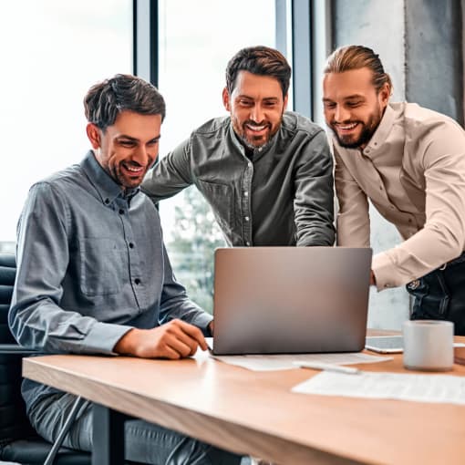 Three young professionals smiling and discussing while looking at a laptop screen.
