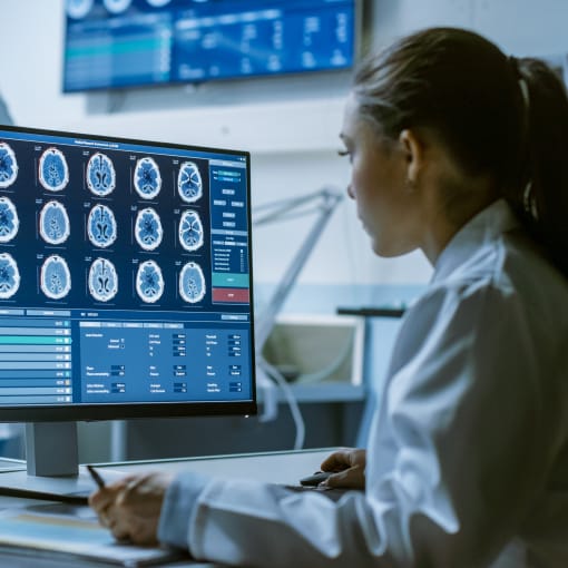 A woman in a doctor's coat looking at brain image scans.
