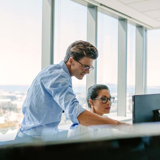 Two coworkers look at dual screens and strategize about future AI projects.