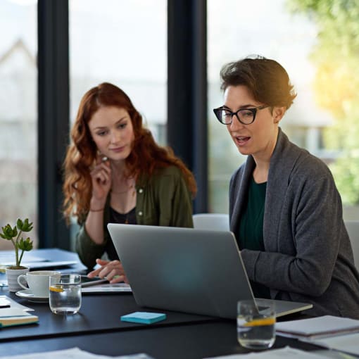 Two coworkers sit at a conference table and collaborate on crafting a business case proposal for migrating to the cloud. 