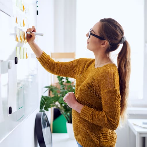 A woman with a ponytail writing on a whiteboard.