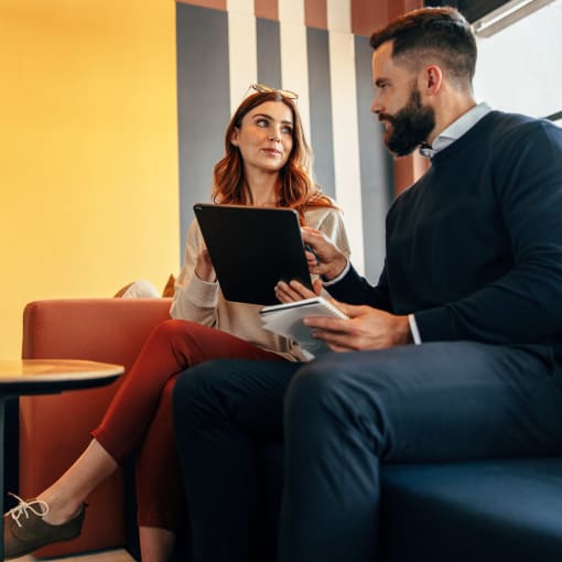 Two coworkers sitting on a couch, looking at a laptop