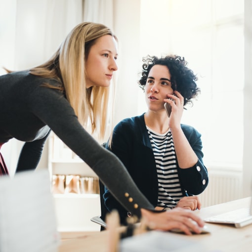 Two female colleagues at a desk talking