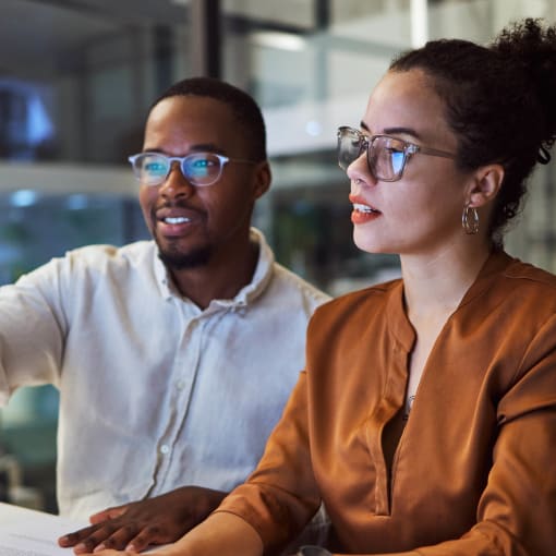 Two coworkers sit at a desktop computer and explore the differences in AI and machine learning.