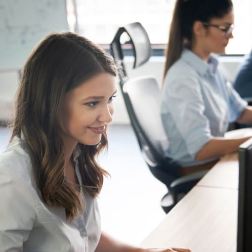 Two people sit and type on computer keyboards in an office setting.