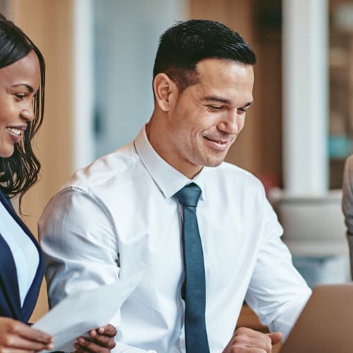 Two people stand, smile and look at a laptop.