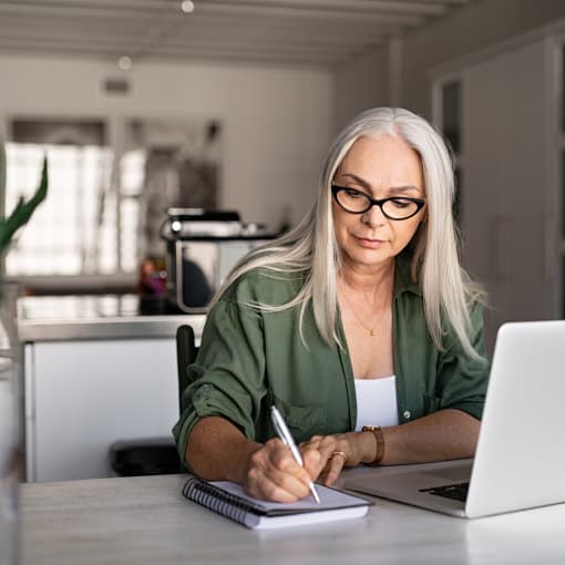 A person sitting in front of their laptop writing down notes with a pen.