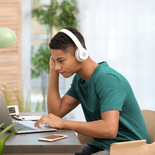 A young person wearing headphones and sitting in front of a laptop studying.