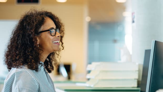 Person in glasses at a desk in an office works at a computer.