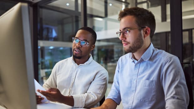 Two young professionals collaborate at a desktop computer.