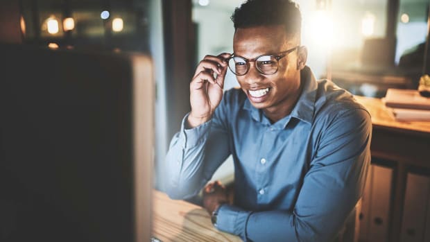 An employee at their desk in an office setting, smiling at their desktop monitor as if talking on a video call.