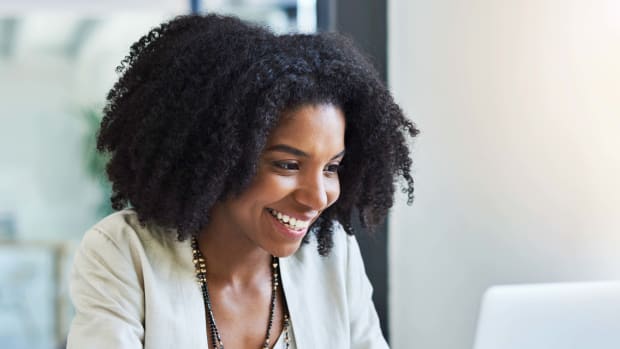 Person smiles while working at a white laptop.