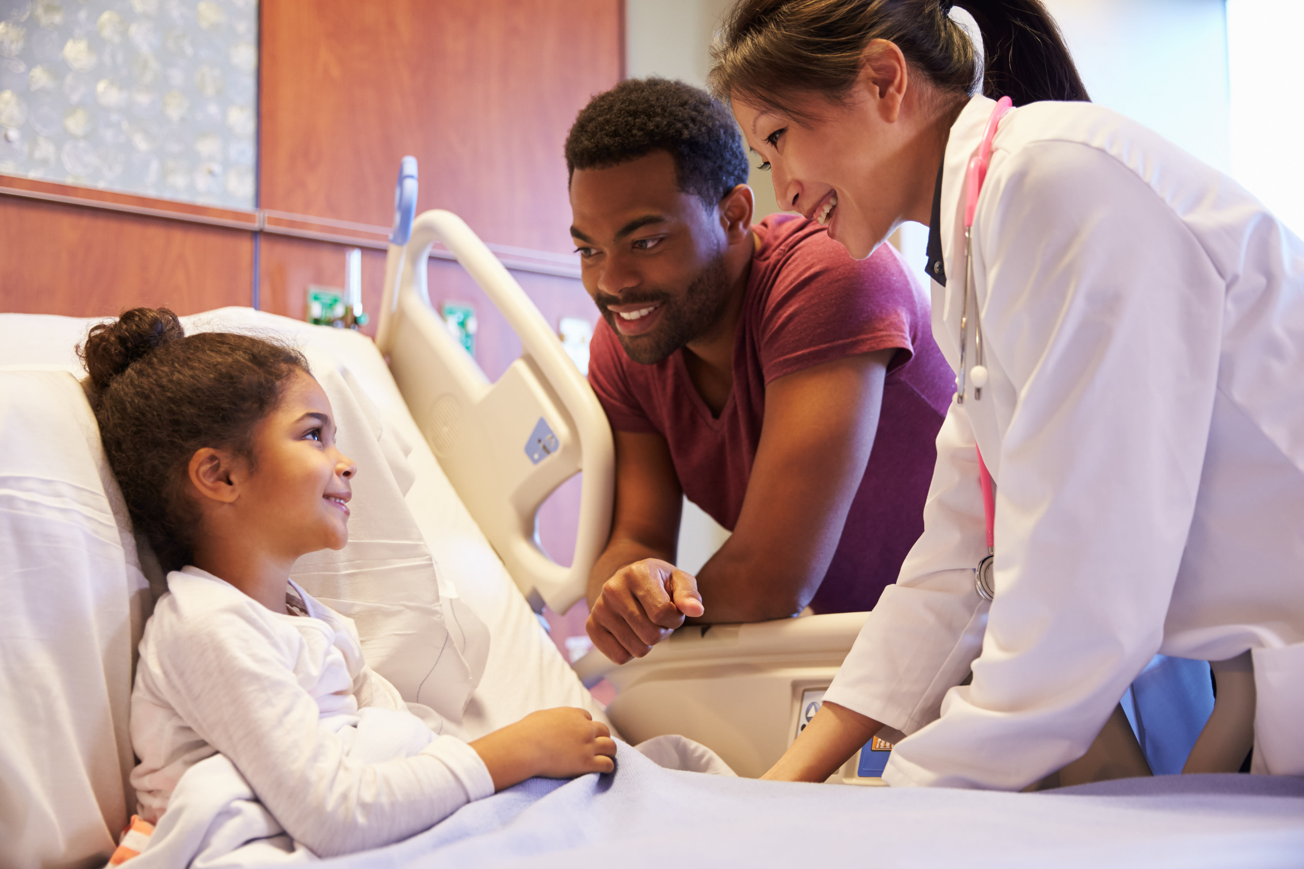 Child in a hospital bed with nurse and caregiver