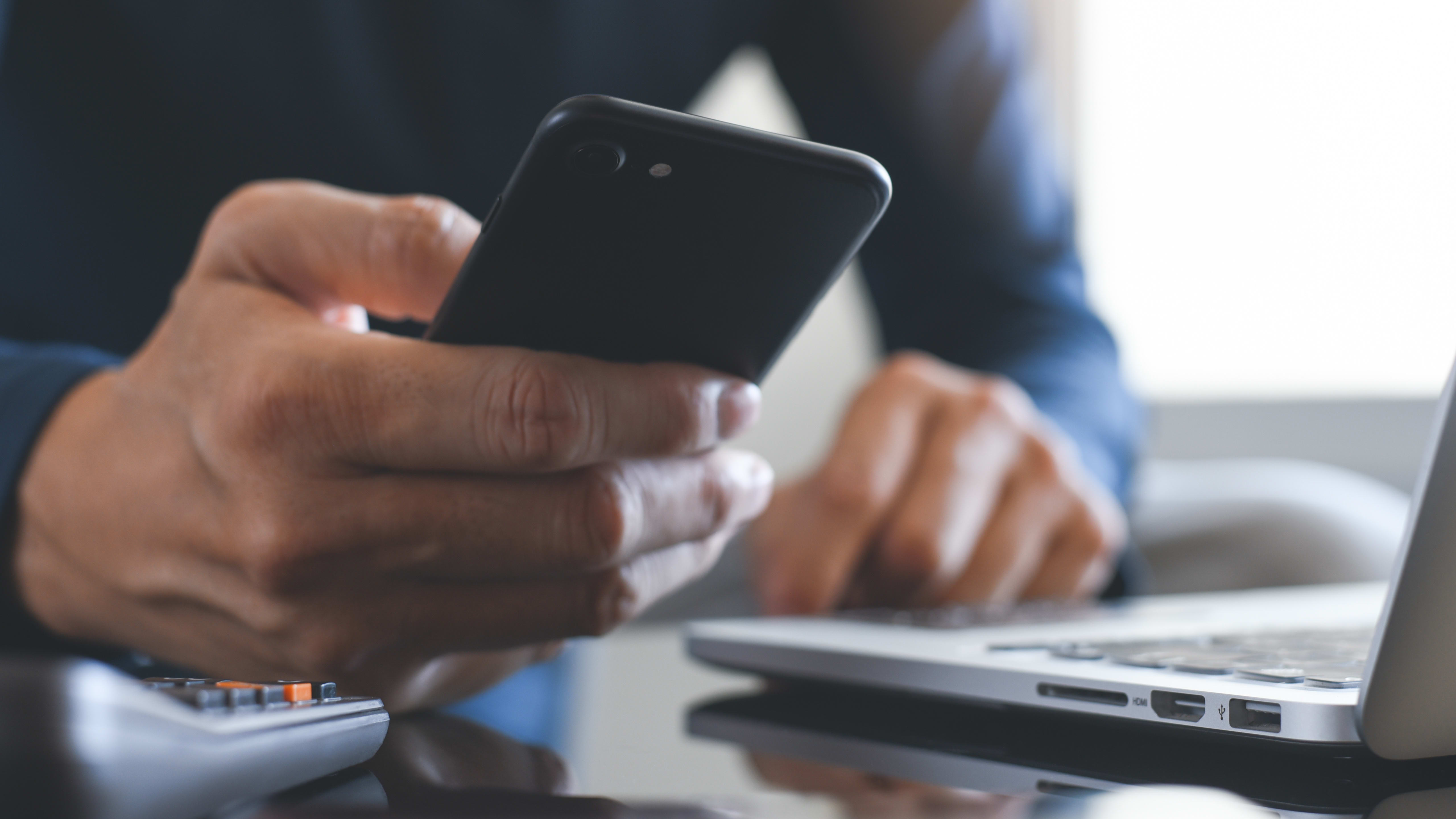 Close photo of a person holding a cell phone while working on a laptop.
