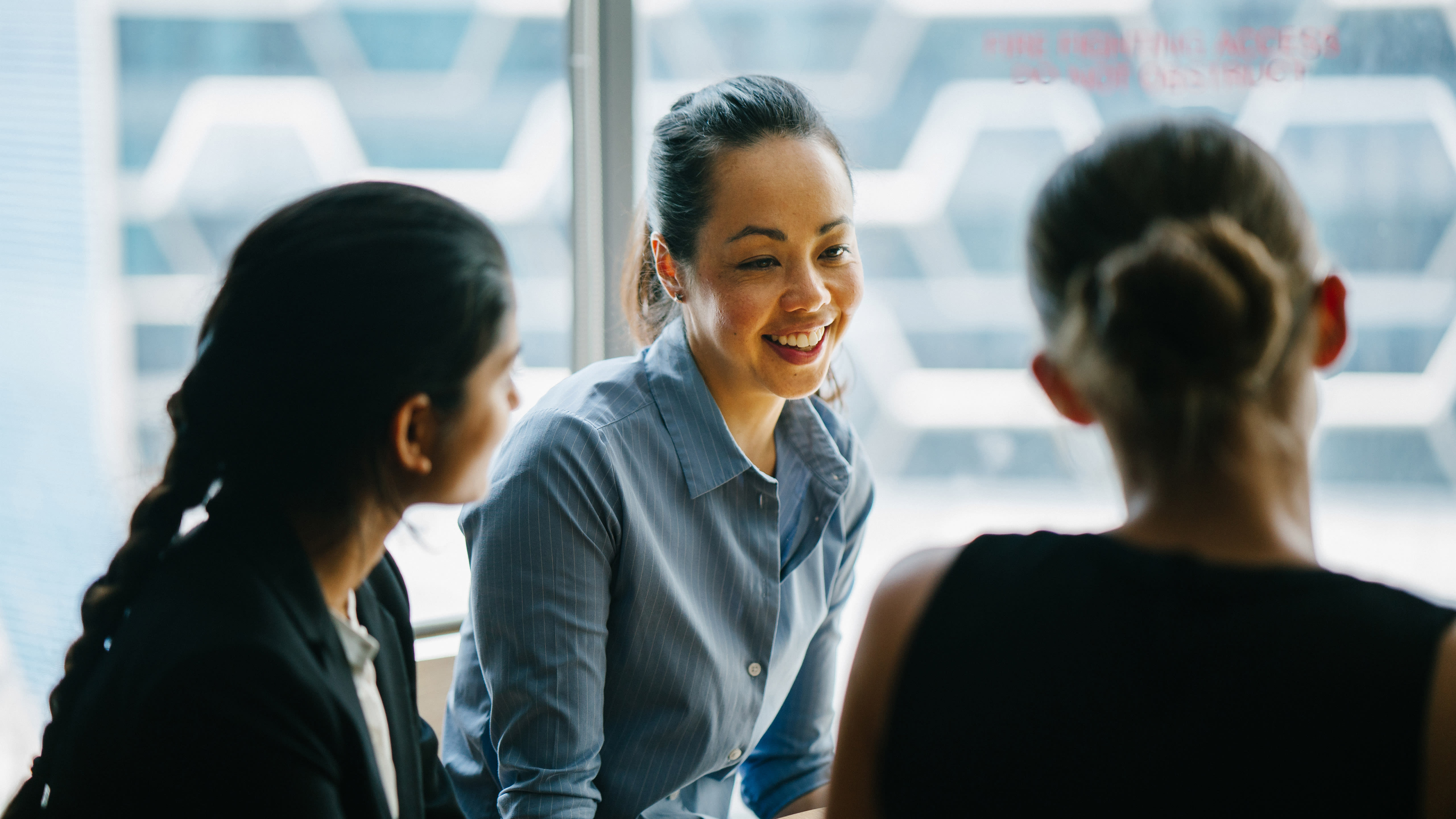Three young professionals talk together in front of a frosted glass window.
