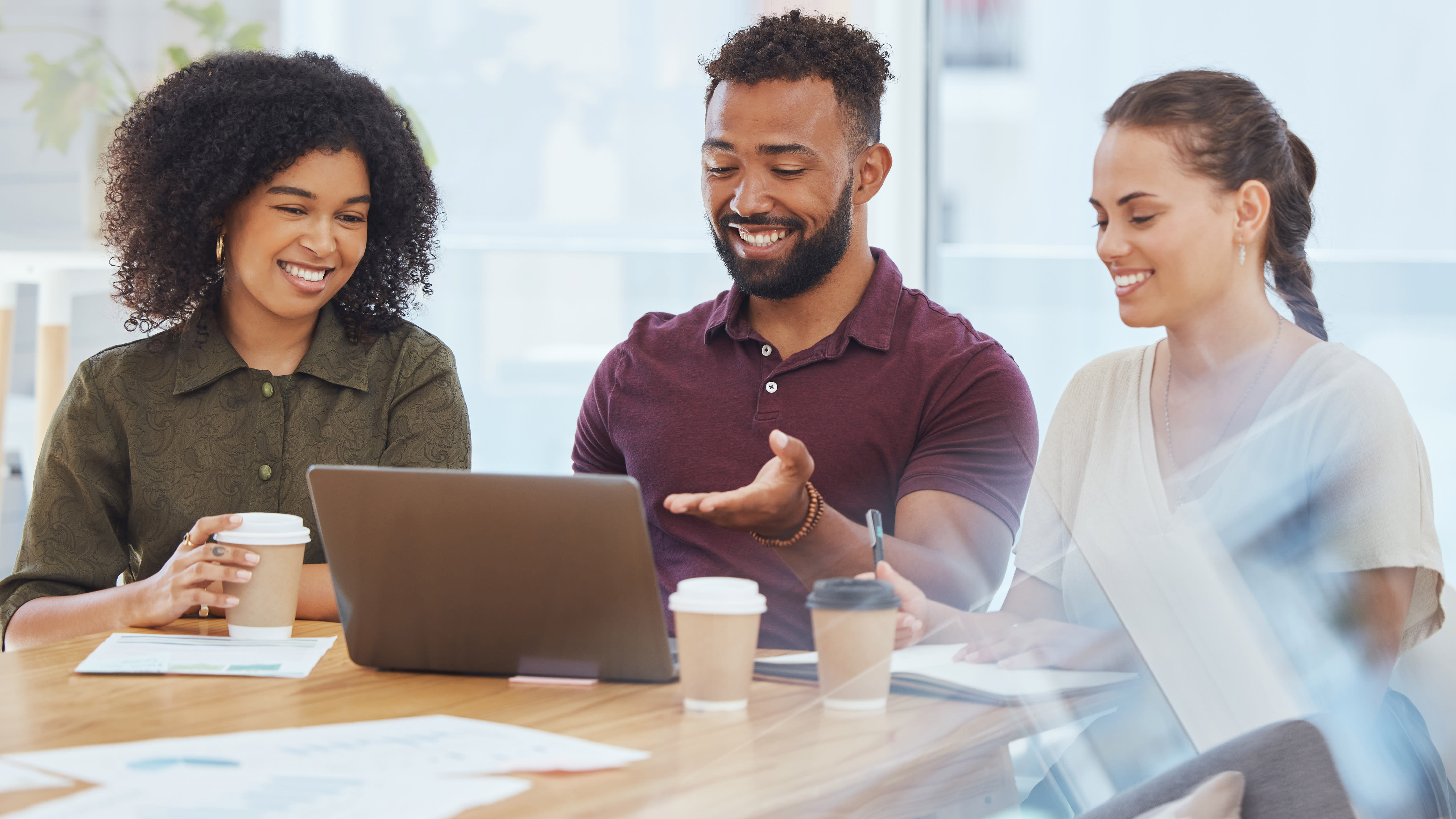 Three co-workers sit at a conference desk with coffee and a single laptop to strategize their intelligent automation strategy.