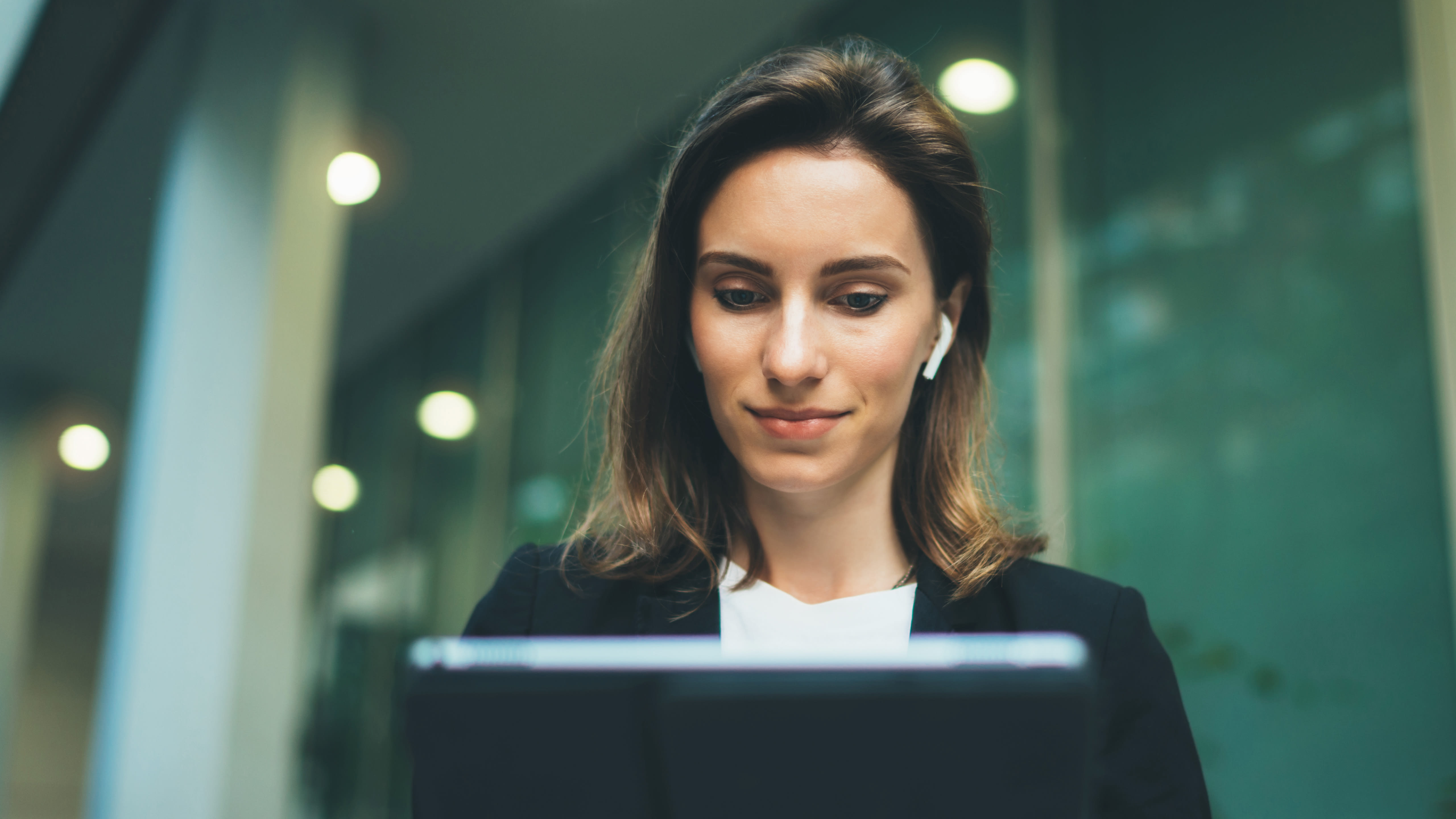 An employee with earbuds works on their laptop in an office building.