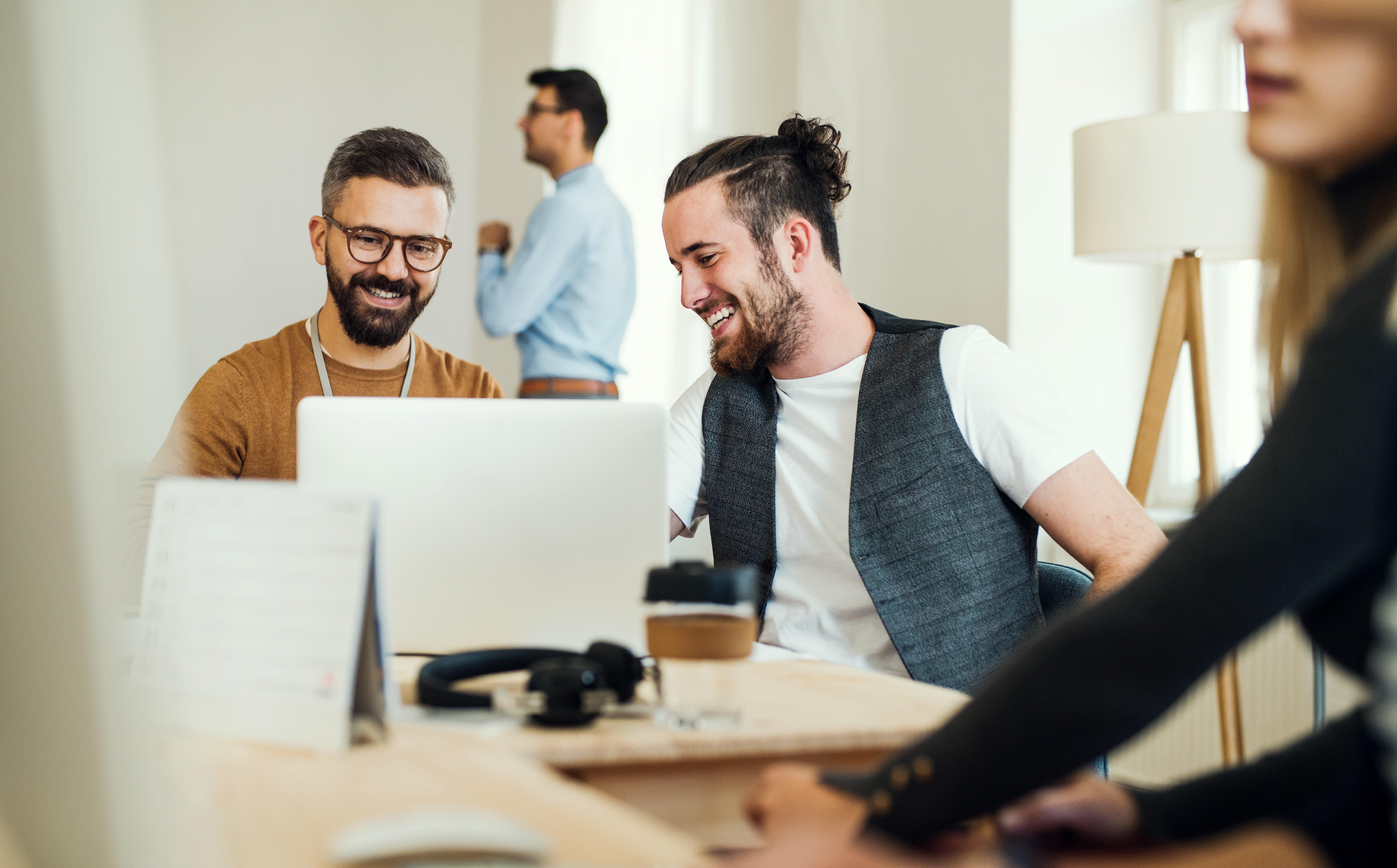 Two people smile and look at information on a laptop. There are headphones on the table.