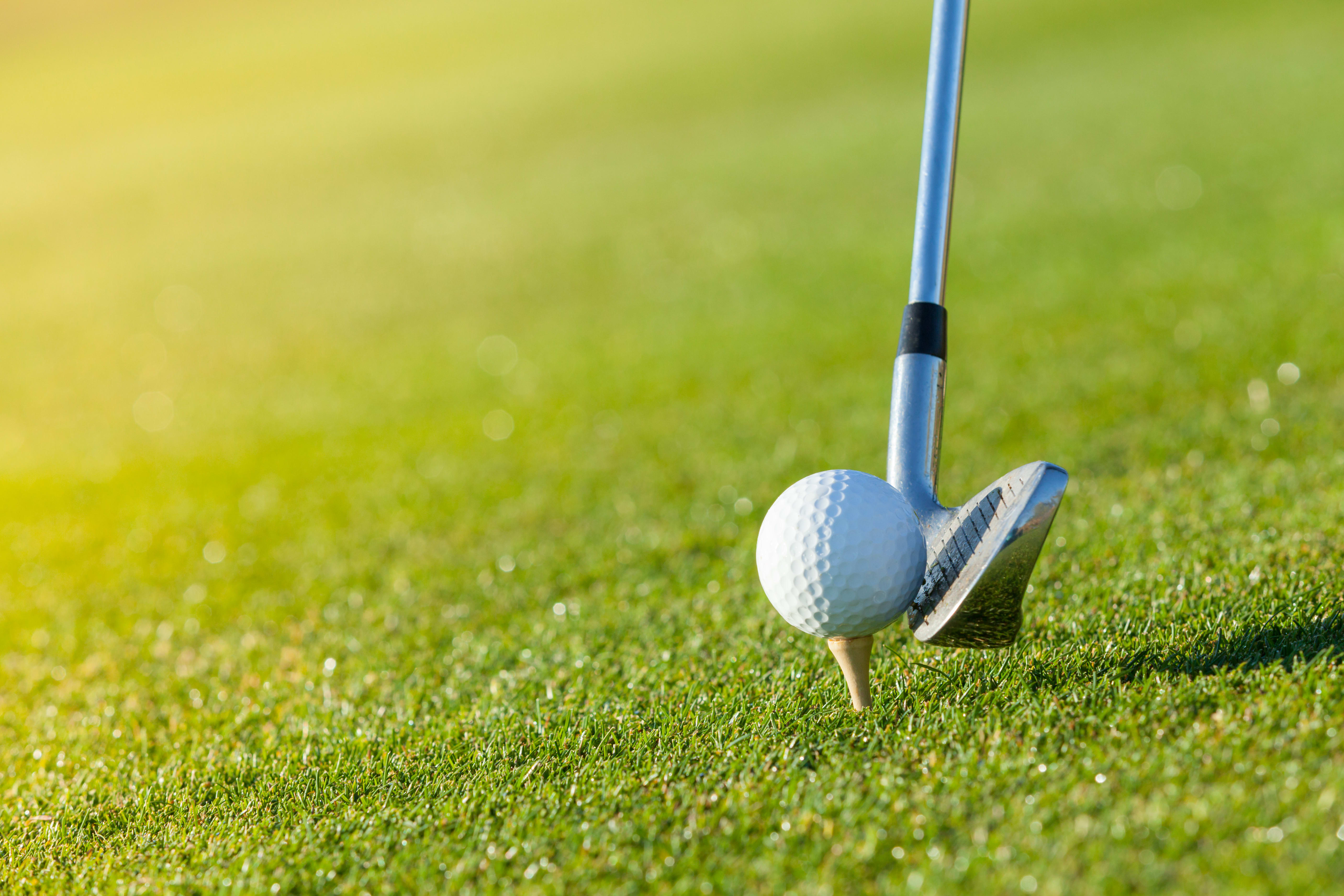 A golf club prepares to hit a ball on a tee.