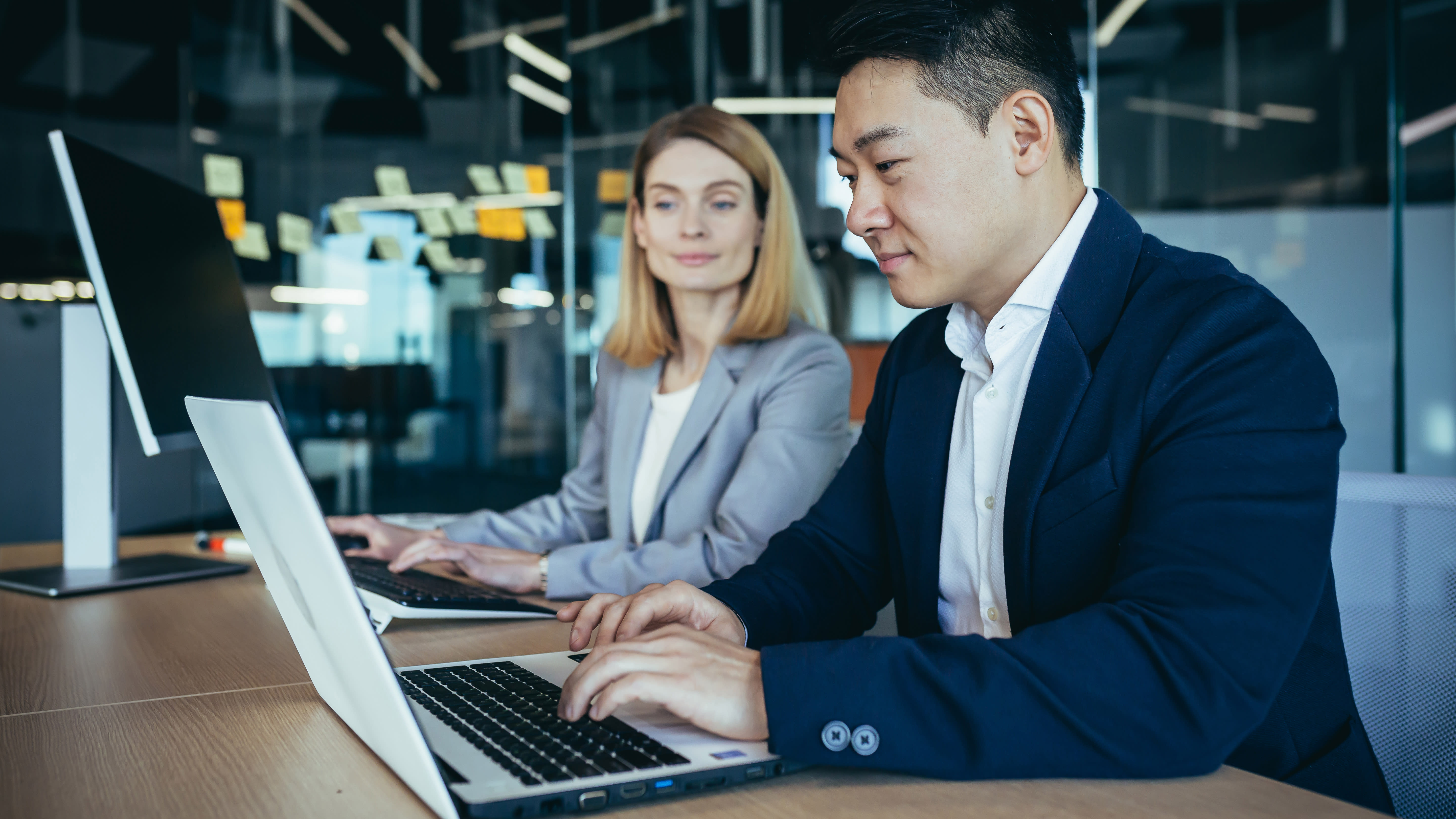 Two businesspeople in suits sit at laptops.