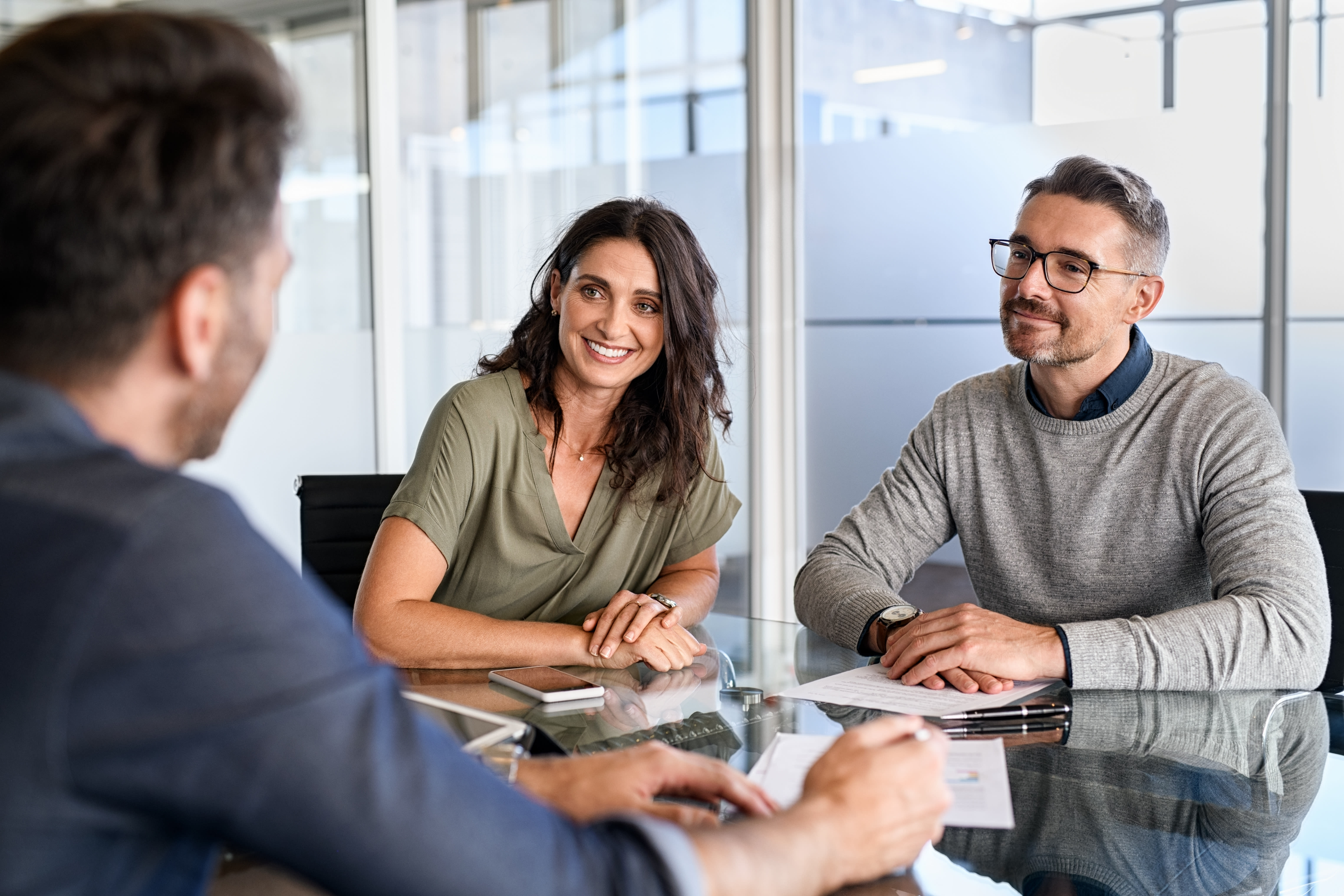 Two people smile and talk as they sit in an office. There is a mobile phone on the table. 