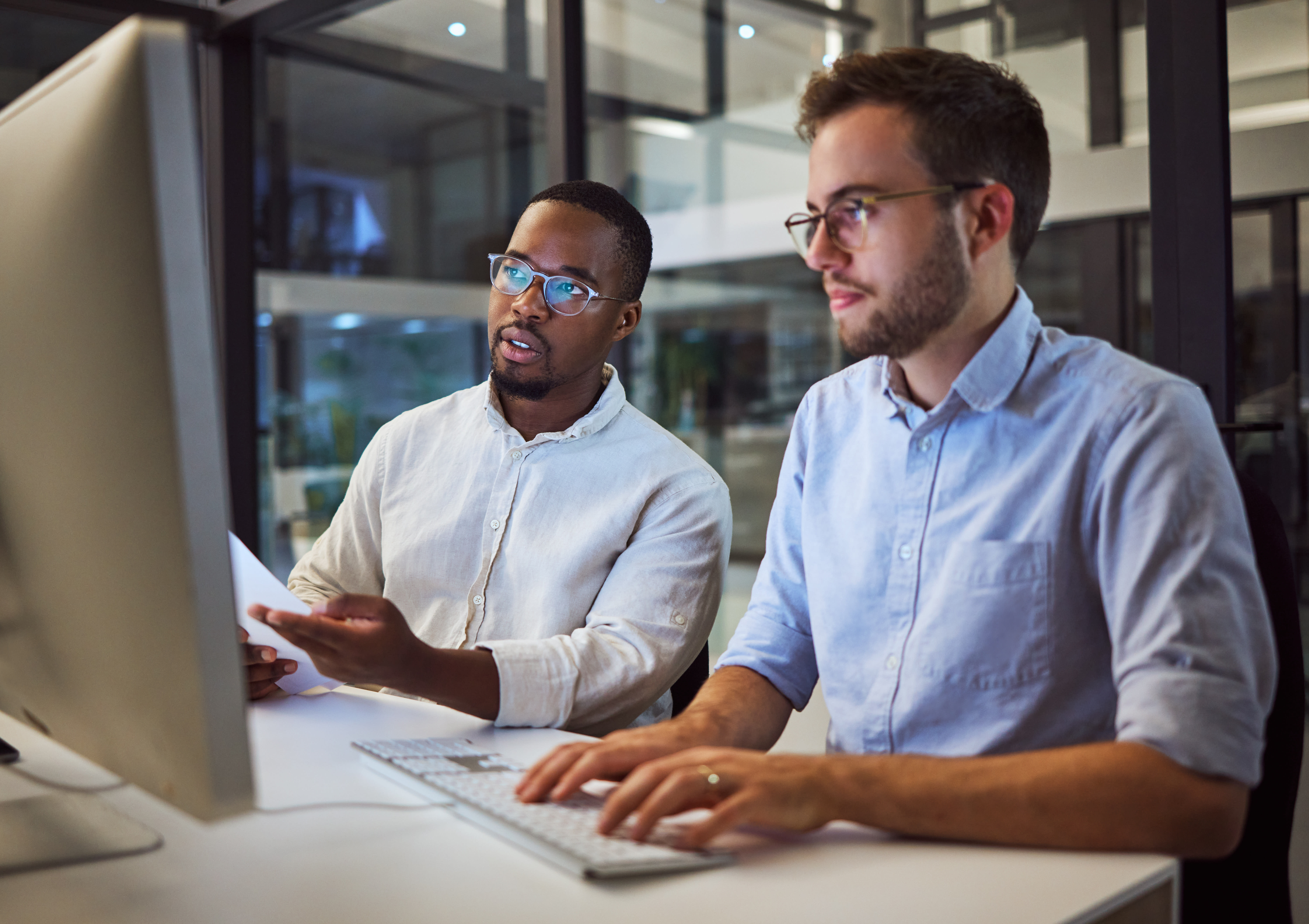 Two business professionals sit side-by-side collaborating at a computer while one types.