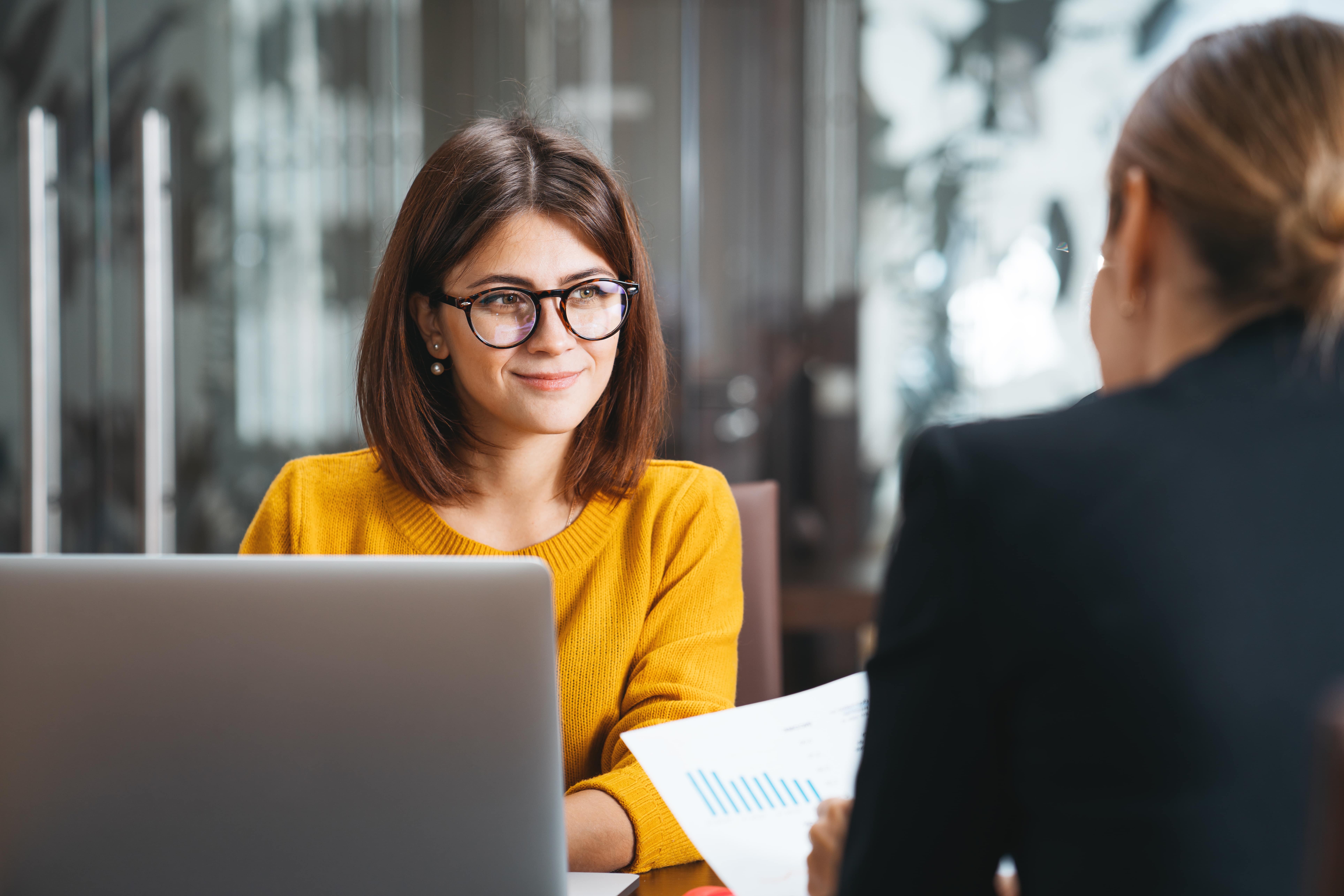 Two people in an office setting sit at a desk, reviewing metrics in a bar graph.