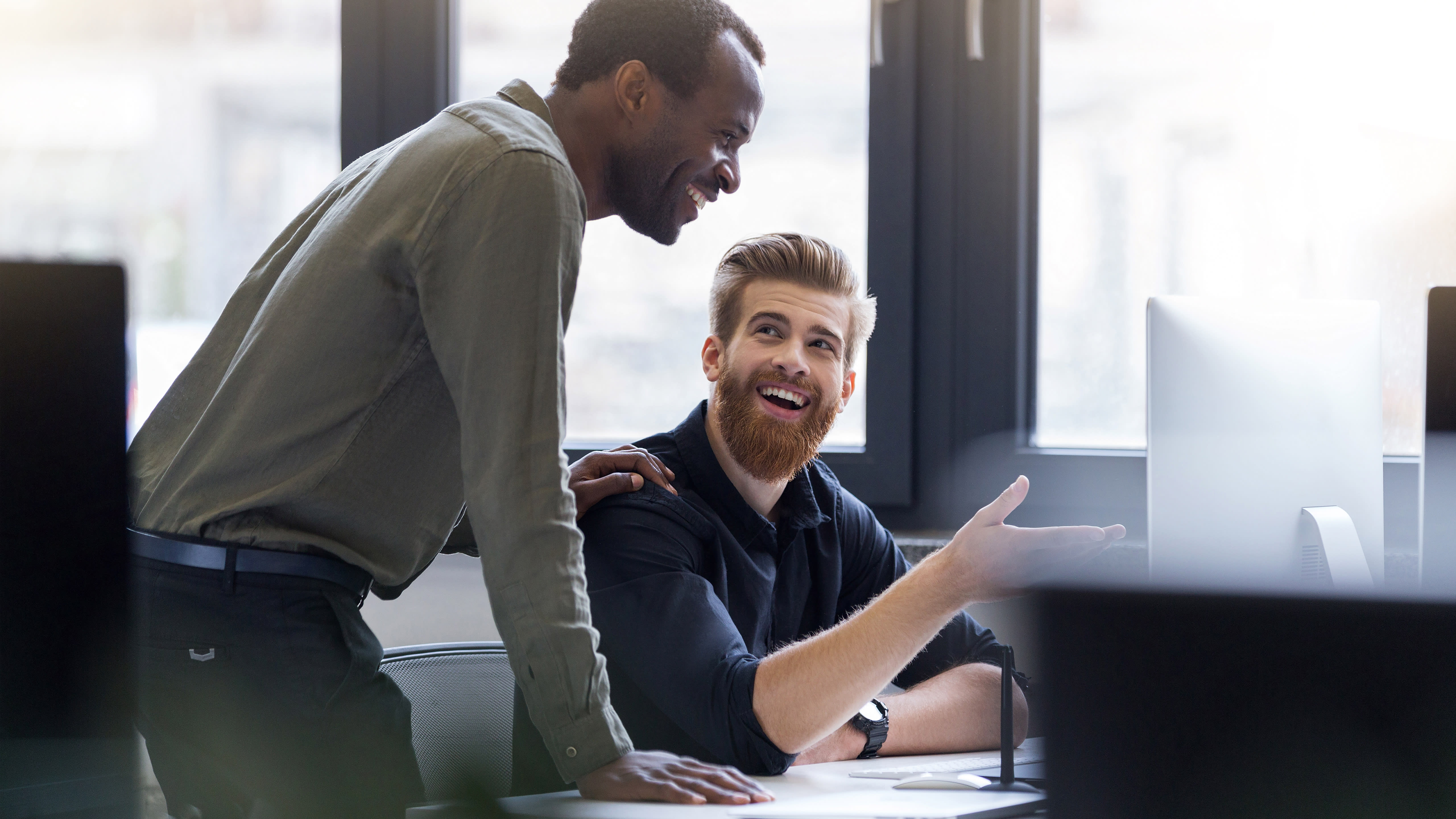 Two colleagues collaborate at a desktop computer in an office.