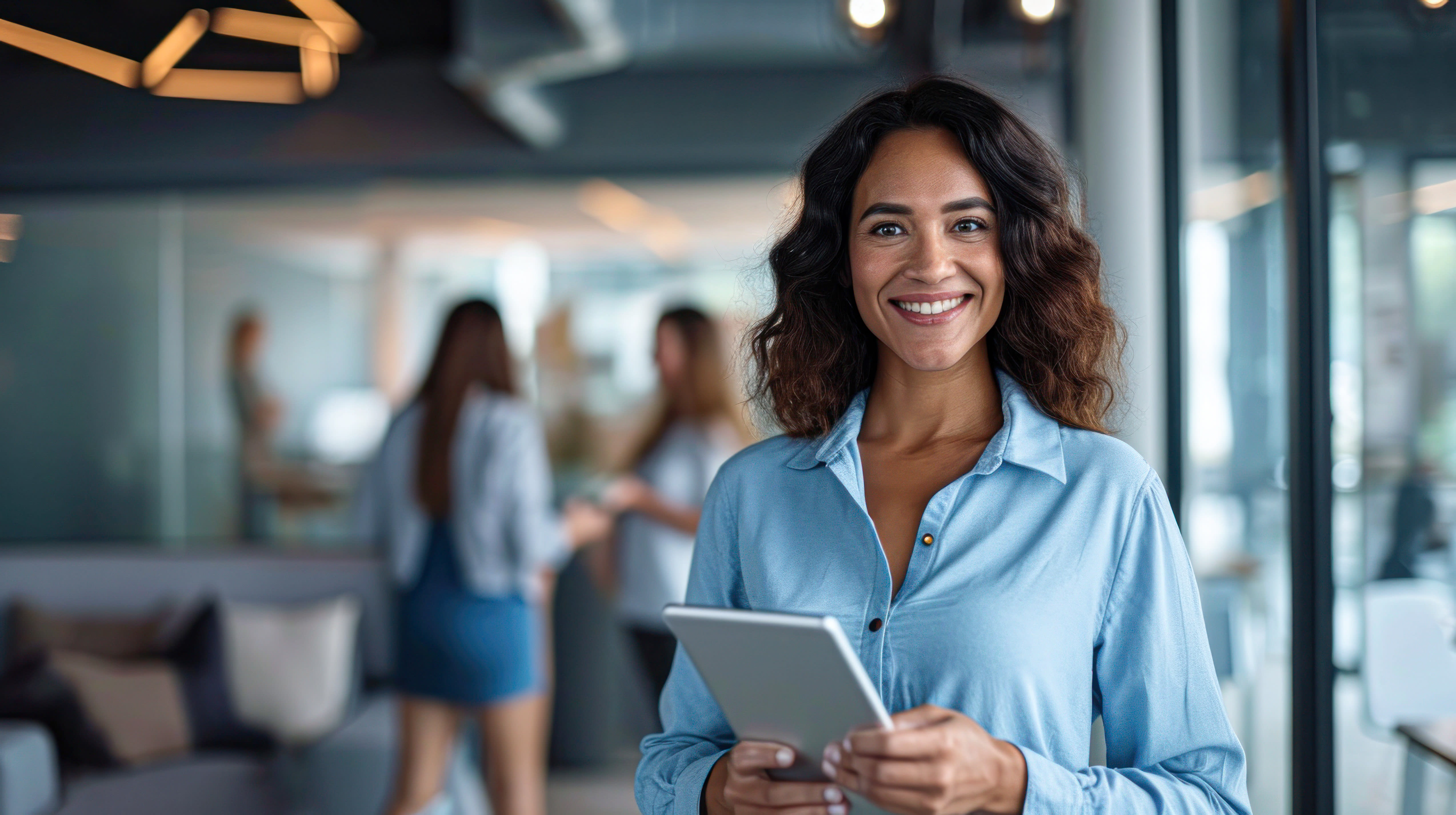 Woman in blue shirt holding a tablet next to a window