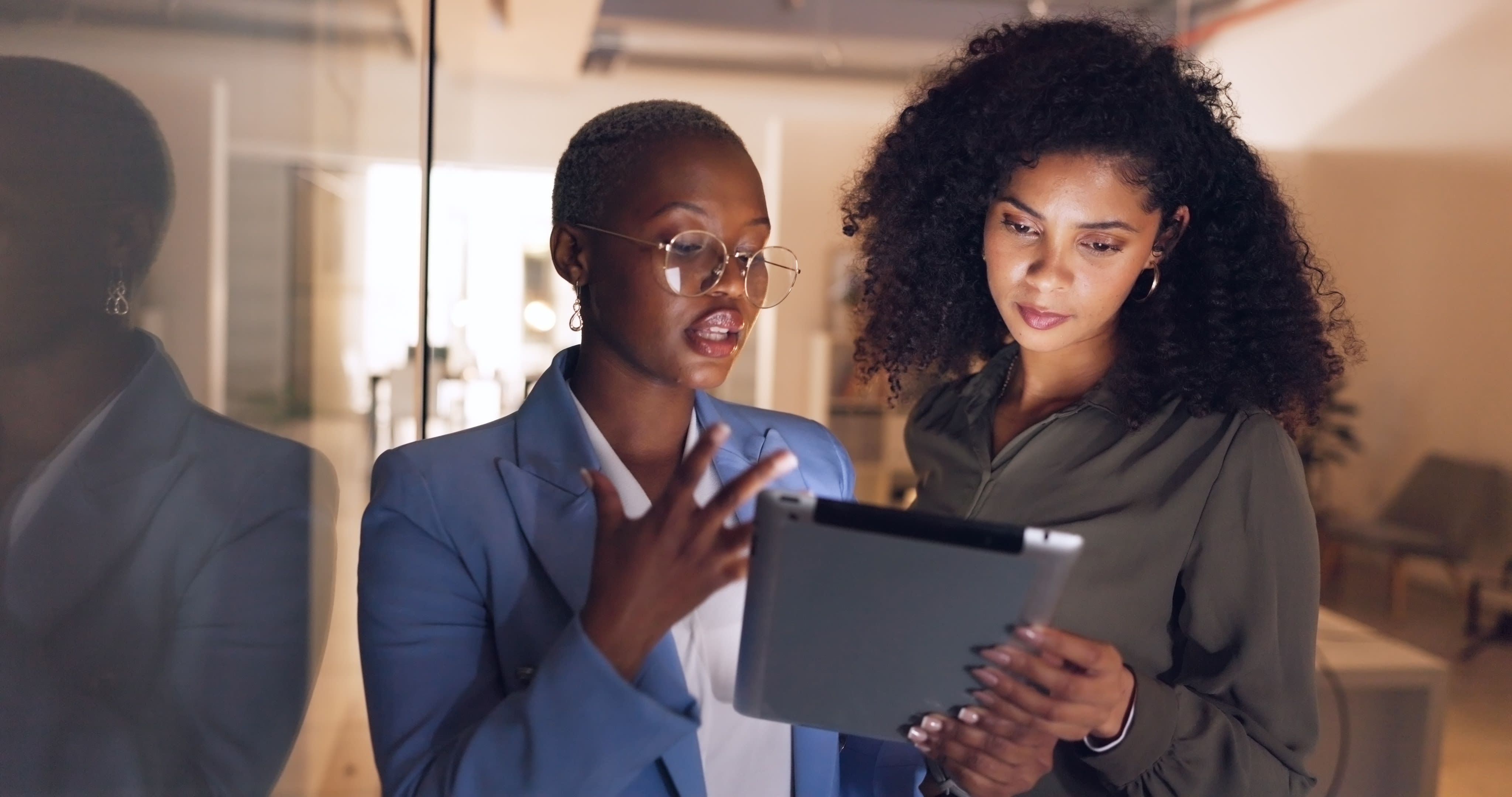 Two women looking at a tablet and having a business discussion at an office.