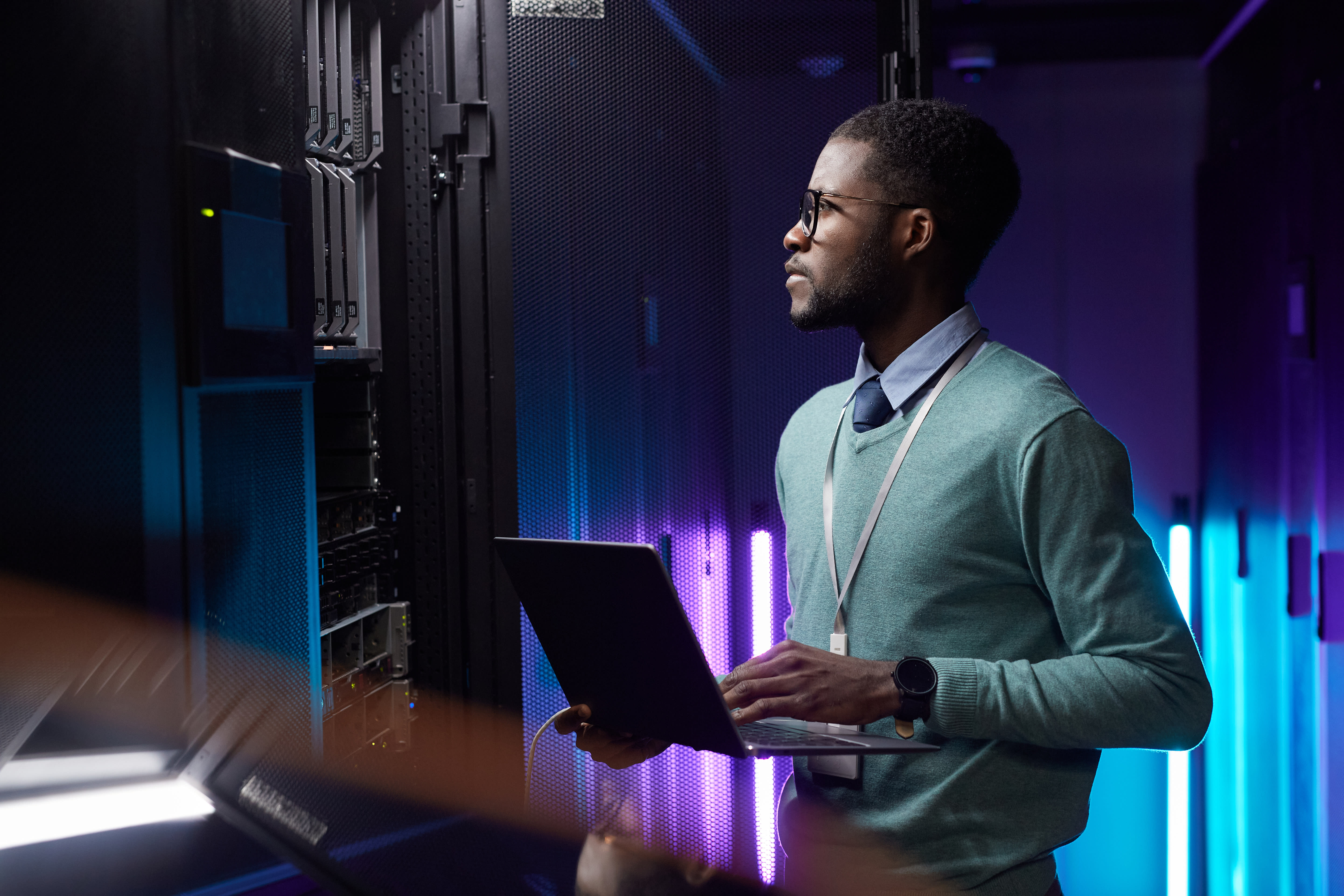 Man with glasses in server room with laptop