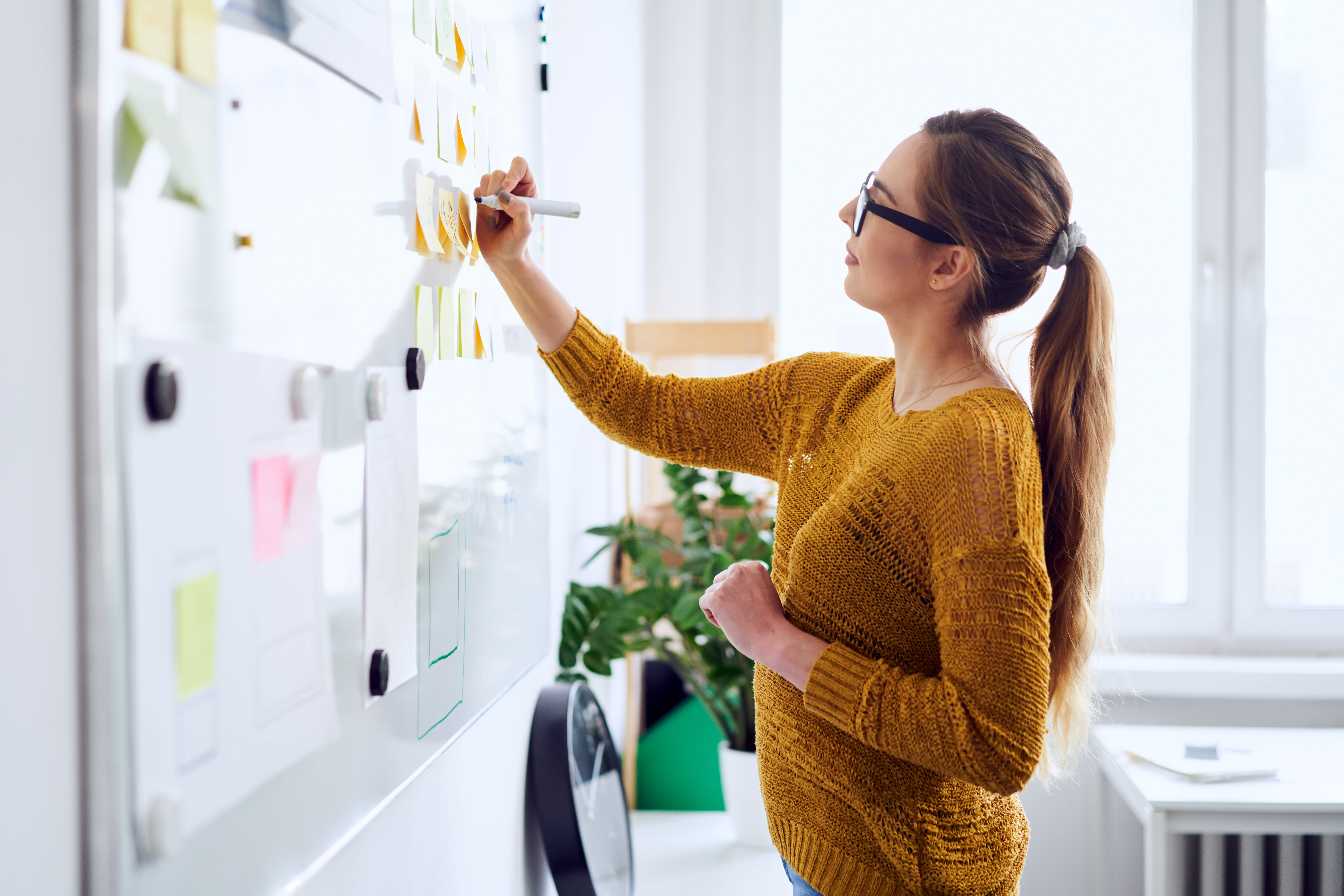 A woman with a ponytail writing on a whiteboard.
