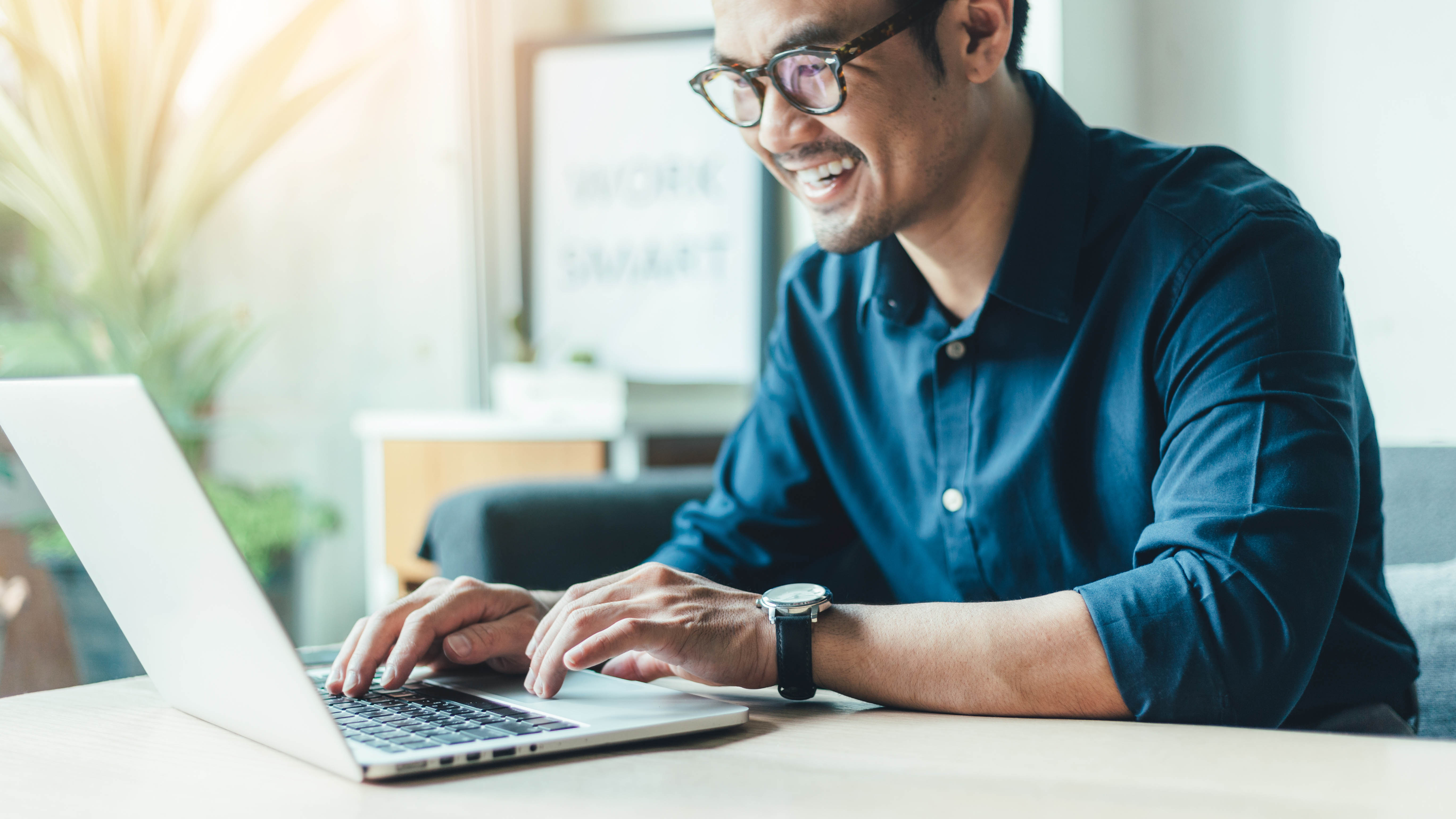 Person in blue button-down shirt works on laptop at a table.