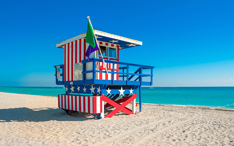 Torre de salvavidas con diseño patriótico en la arena blanca de South Beach, Miami, destino popular entre los viajeros de Travel Club Agencia de Viajes