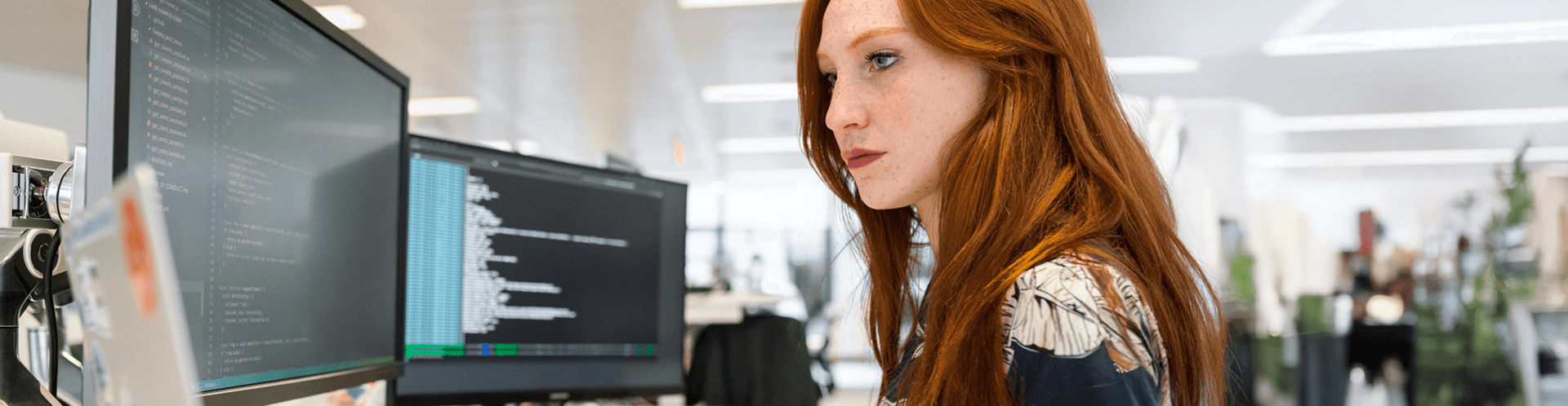 Frau programmiert an zwei Monitoren.