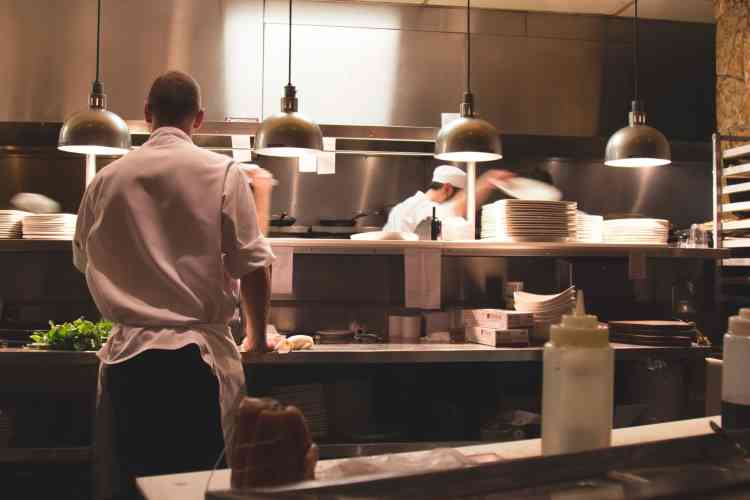 A busy restaurant kitchen scene with chefs working rapidly behind the pass, highlighting the intensity of kitchen operations.