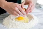 cracking an egg into flour to make homemade pasta dough | Classpop Shot