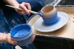 a woman painting a pottery vase with blue paint Shot