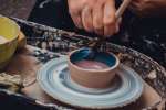 a woman painting a pottery vase in blue Shot